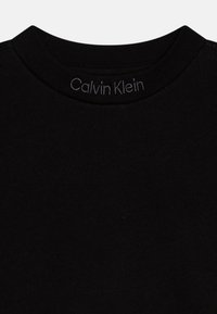 Melnas kokvilnas T-krekls ar ribotu apkakli. "Calvin Klein" logo izšūts pelēkā krāsā pie apkakles. Mīksta tekstūra, standarta piegriezums.