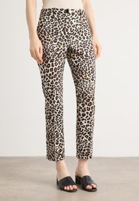 Pantalons en imprimé léopard en tissu léger avec une coupe ajustée, présentant des nuances de noir, marron et crème, associés à des talons ouverts noirs.