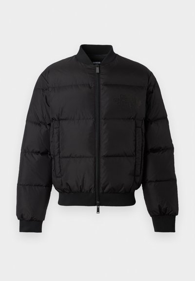 Zwarte pufferjack met een ritssluiting aan de voorkant, ribgebreide manchetten en zoom. Beschikt over een gewatteerd ontwerp en tonaal merk op de linkerkant van de borstzak.