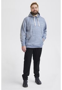 Hoodie bleu clair chiné avec une capuche à cordon, poche avant et ourlet côtelé, associé à un pantalon noir fuselé et des chaussures foncées.