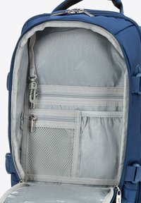 Interiér modrého batohu s šedým podšíváním; obsahuje zipové kapsy, síťovou kapsu a hladkou texturu látky. Zipové uzavření na vrchu.