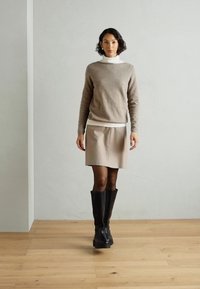 Maglione beige lavorato a maglia, dolcevita bianco sotto, gonna beige, stivali neri sopra il ginocchio. Texture lisce, design minimalista, colori tenui.