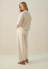 Pull en beige clair avec des motifs de pois bruns, associé à un pantalon large de couleur crème. Les chaussures présentent un design à imprimé léopard.