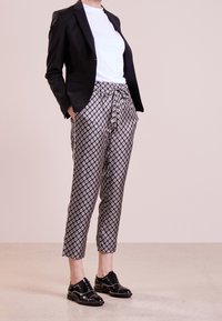 Černý blazer přes bílý tričko, v kombinaci s vzorovanými zkrácenými kalhotami s diamantovým vzorem v černé a bílé, a černými šněrovacími botami.