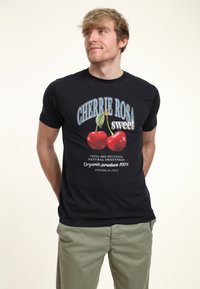 Camiseta negra con un gráfico de cereza. El texto dice "CHERRIE ROSA dulce" con detalles sobre productos orgánicos cultivados en Italia. Mangas cortas, diseño ajustado.