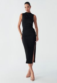 Robes noires sans manches au design ajusté, avec des fronces sur le côté et une fente haute. Tissu doux avec une texture minimale et une silhouette élégante.