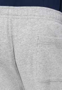 Szare dresowe spodnie z materiału o fakturowanej powierzchni, elastyczną talią i boczną kieszenią. Zbliżenie na detale szwów i wzory tkaniny.