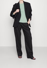 Zwarte op maat gemaakte blazer over een lichtgroene kabelgebreide trui, gecombineerd met losse zwarte broek en eenvoudige zwarte sandalen.