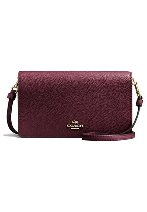 Bolso bandolera de piel texturizada en rojo oscuro con logo dorado de Coach y correa ajustable con cierres dorados.