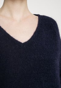 Pull bleu marine en V, fabriqué en tissu tricoté doux et texturé, avec une coupe légèrement ample, mettant en avant un design minimaliste.