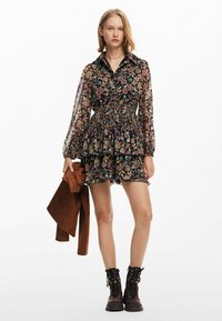 Blommönstrad klänning med ett veckat midja, genomskinliga långärmade ärmar och volangkant. Kombinerad med en brun mockajacka och svarta snörstövlar.