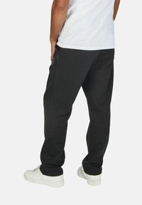 Black sweatpants made of cotton blend fabric, featuring side pockets, elastic waistband, and a tapered leg design. Worn with white sneakers.
