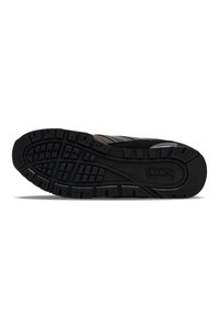 Black athletic shoe sole with textured rubber for grip, featuring deep treads and a curved design. Simple branding on the footbed.