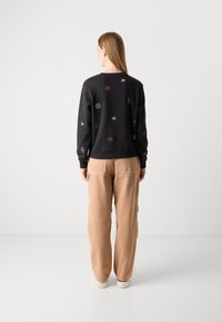 Felpa nera con motivi ricamati multicolori, abbinata a pantaloni cargo beige. Tessuto morbido, vestibilità comoda, polsini e orlo a coste.