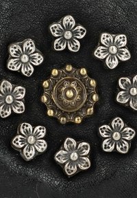 Decorazioni metalliche floreali argentate con motivi dettagliati, che circondano un pezzo decorativo centrale in tono dorato, il tutto su uno sfondo nero testurizzato.