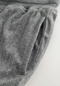 Grau gewebter Stoff im Fischgrätmuster mit weicher Textur und Faltendetails, sowie einem glatten Bund oben.
