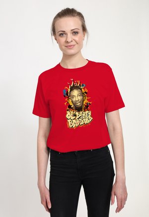 Vrouw die een rood T-shirt draagt met een kleurrijke afbeelding van een mannengezicht en de tekst "Ol' Dirty Bastard" in gestileerde letters.