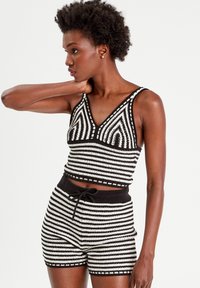Zwart-witte gestreepte crop top en shorts set, gemaakt van textuurstof, met een V-halsontwerp en decoratieve accenten op de top.