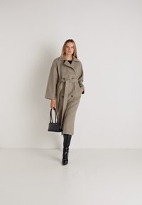 Abrigo envolvente de lana beige con cinturón, cierre de doble botonadura, mangas anchas y cuello con muesca. Combinado con botas negras hasta la rodilla y un bolso negro.