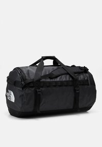 Svart duffelbag laget av slitesterkt stoff, med justerbare skulderstropper, responsive spenner, og The North Face-logoen på siden.
