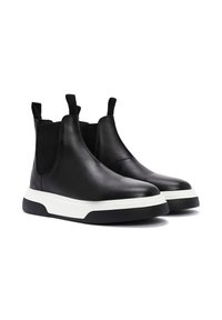Botas Chelsea de cuero negro con paneles laterales elásticos, puntera redondeada y una suela de goma blanca para contraste. Acentos texturizados en las áreas elásticas.