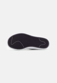 Sola de sapatilha branca com sola de borracha preta texturizada, apresentando um padrão em zig-zag e linhas curvas para melhor aderência e flexibilidade.