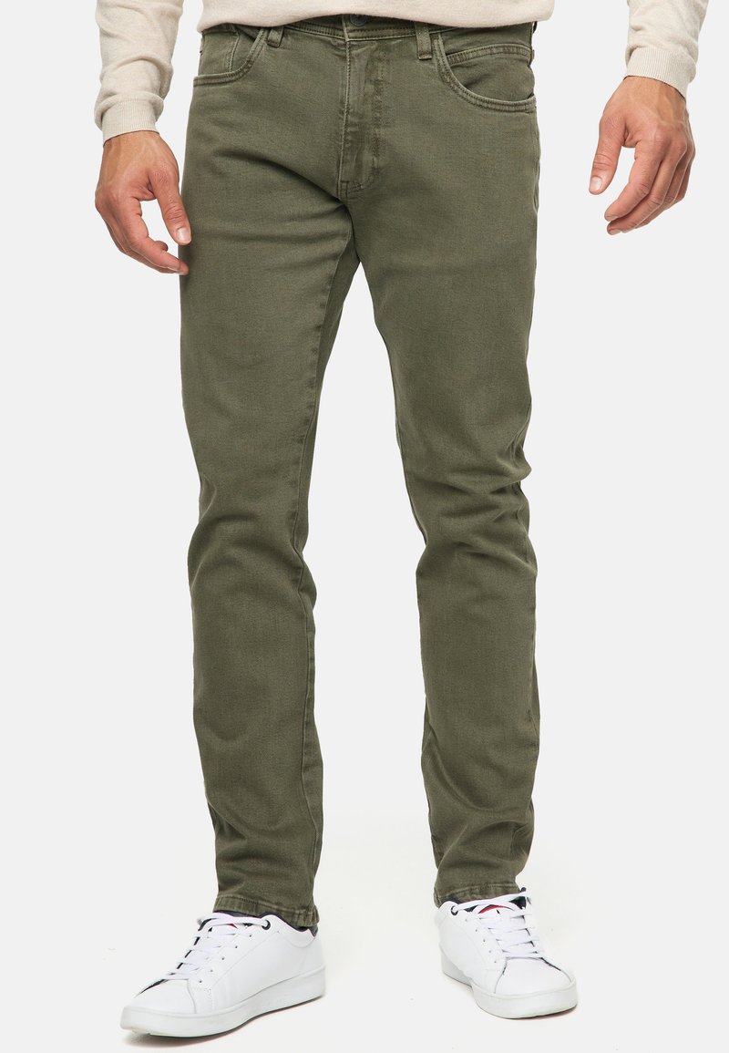 Pantalones vaqueros verde oliva de mezcla de algodón, de corte ajustado, con cinco bolsillos y trabillas para cinturón; combinados con zapatillas blancas.