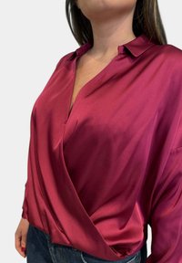 Blusa di seta in un profondo bordeaux, con scollatura a V e design avvolgente. Tessuto liscio con maniche lunghe e silhouette rilassata.