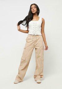Vitt snörat croptop i spets kombinerat med löst sittande beiga cargobyxor med sidfickor och dragsko i midjan. Casual sneakers fulländar looken.