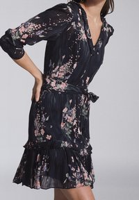 Blommönstrad klänning i svart chiffong, med V-ringning, trekvartsärmar, volangkjol och midjehögt band för att betona midjan.
