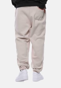 Lyse beige sweatpants med en afslappet pasform og elastiske cuffs, der har sidelommer og et blødt, tekstureret stof, parret med hvide sneakers.