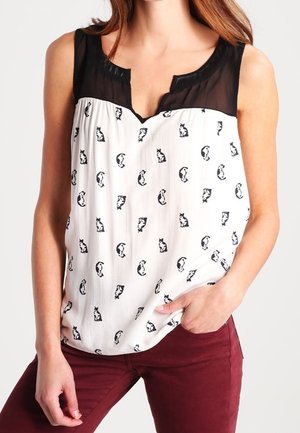 Ärmelloses Oberteil mit einem schwarzen transparenten Ausschnitt, weißem Stoff mit einem schwarzen Katzenmuster und lockerer Passform. Kombiniert mit bordeauxfarbenen Hosen.