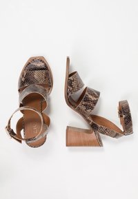 Bruna och svarta högklackade sandaler med ormskinnsmönster, breda remmar, en avsmalnande klack och en texturerad sula. Justerbar vristrem.