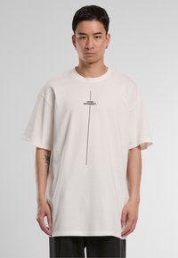 Oversized cream t-shirt made of cotton, featuring a black printed text "THINK DIFFERENT." centered vertically. Short sleeves, crew neck design.