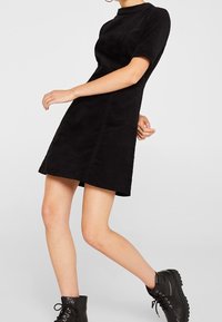 Schwarzes kurzärmeliges Kleid mit taillierter Silhouette, aus strukturiertem Stoff, mit hochgeschlossenem Ausschnitt und dezent ausgestelltem Saum.