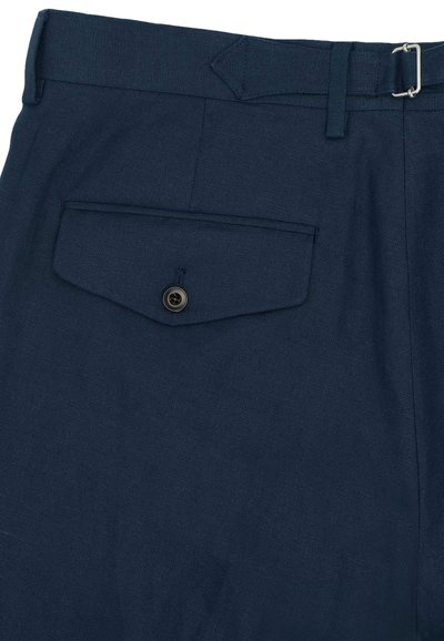 Pantalon bleu marine avec une poche arrière à rabat fermée par un bouton noir et un détail de boucle métallique sur la ceinture.