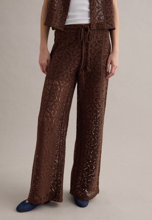 Pantaloni marroni all'uncinetto a gamba larga con vita con coulisse, indossati con un top bianco e scarpe blu, mostrati dalla vita ai piedi.