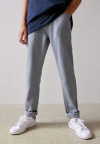 Pantalones de mezclilla gris claro con puños doblados, combinados con zapatillas blancas. La tela parece suave, con un ajuste casual y detalles en la costura lateral.