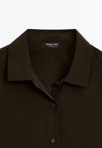 Mørkebrun skjorte med krave og glat overflade, der har en knaplukning og en etiket med teksten "Massimo Dutti" indeni kraven.