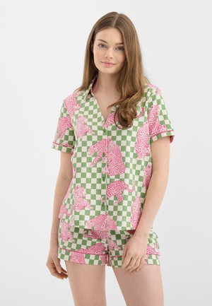 Giovane donna con lunghi capelli castano chiaro indossa un completo composto da camicia a maniche corte a quadri verdi e bianchi e pantaloncini con stampa leopardata rosa.