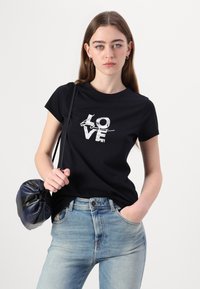 Fekete pamut póló, texturált fehér "LOVE" grafikával, világoskék farmernadrággal és sötétkék, kerek táskával párosítva.