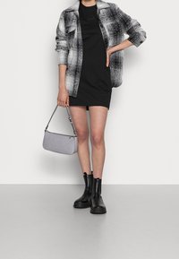 Svart klänning med en rutmönstrad grå och vit övertröja, tillsammans med svarta ankelboots och en grå handväska i krokodiltextur.