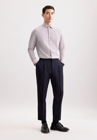 Camicia a righe con bottoni in viola chiaro e bianco, abbinata a pantaloni plissettati blu navy scuro e scarpe nere, su uno sfondo chiaro.