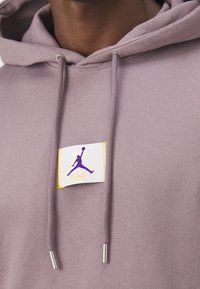 Felpa viola con cappuccio e lacci con estremità metalliche, la patch in evidenza mostra un logo Jumpman viola e il testo "Flight" su uno sfondo bianco.