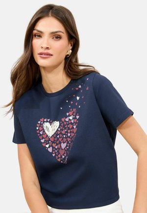 T-shirt in cotone blu navy con un design a forma di cuore composto da vari piccoli cuori nelle tonalità di rosa, bianco e rosso, con la scritta "Hai bisogno di un po' d'amore."