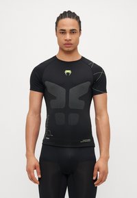 Camiseta deportiva negra de manga corta con un patrón geométrico texturizado en la parte frontal, que presenta acentos en amarillo neón y un diseño ajustado.