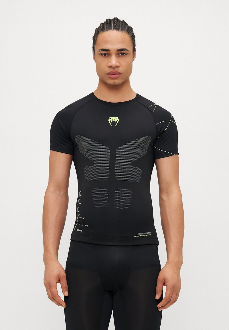 Camiseta deportiva negra de manga corta con un patrón geométrico texturizado en la parte frontal, que presenta acentos en amarillo neón y un diseño ajustado.
