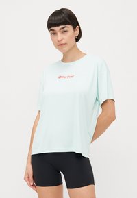 Ljus mintgrön t-shirt med korta ärmar och avslappnad passform, med en röd "Rip Curl"-logotyp på bröstet, tillsammans med svarta shorts.