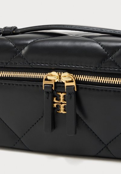 Κοντινό πλάνο μαύρης δερμάτινης τσάντας με καπιτονέ σχέδιο που δείχνει χρυστό φερμουάρ με δύο τζέρτζελα και χρυσό λογότυπο κάτω από το φερμουάρ.