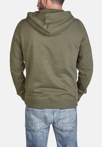 Felpa verde oliva con una vestibilità comoda, cappuccio ampio e polsini e orlo a costine; mostrata indossata con jeans blu sbiaditi vista da dietro.